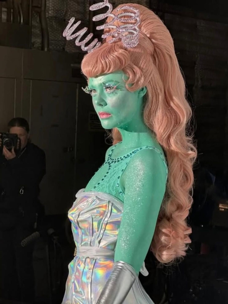 Elle Fanning on the set of Margo's Got Money Troubles dressed as an alien with green skin a silver dress and a pink wig.
